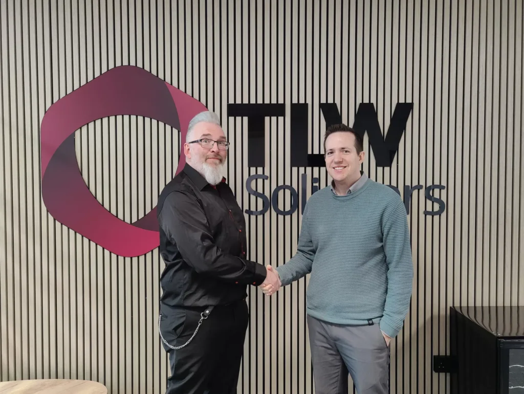 Two men shaking hands in front of Smart IT logo at TLW Solicitors.