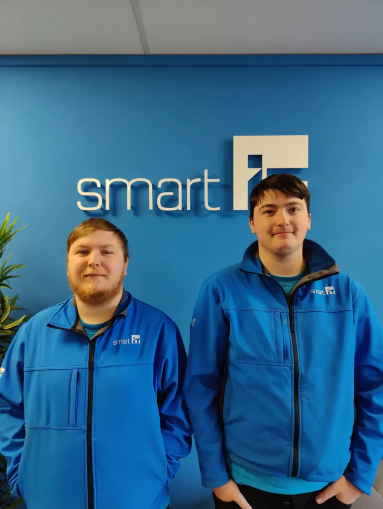 Two team members in blue Smart IT jackets standing in front of company logo.