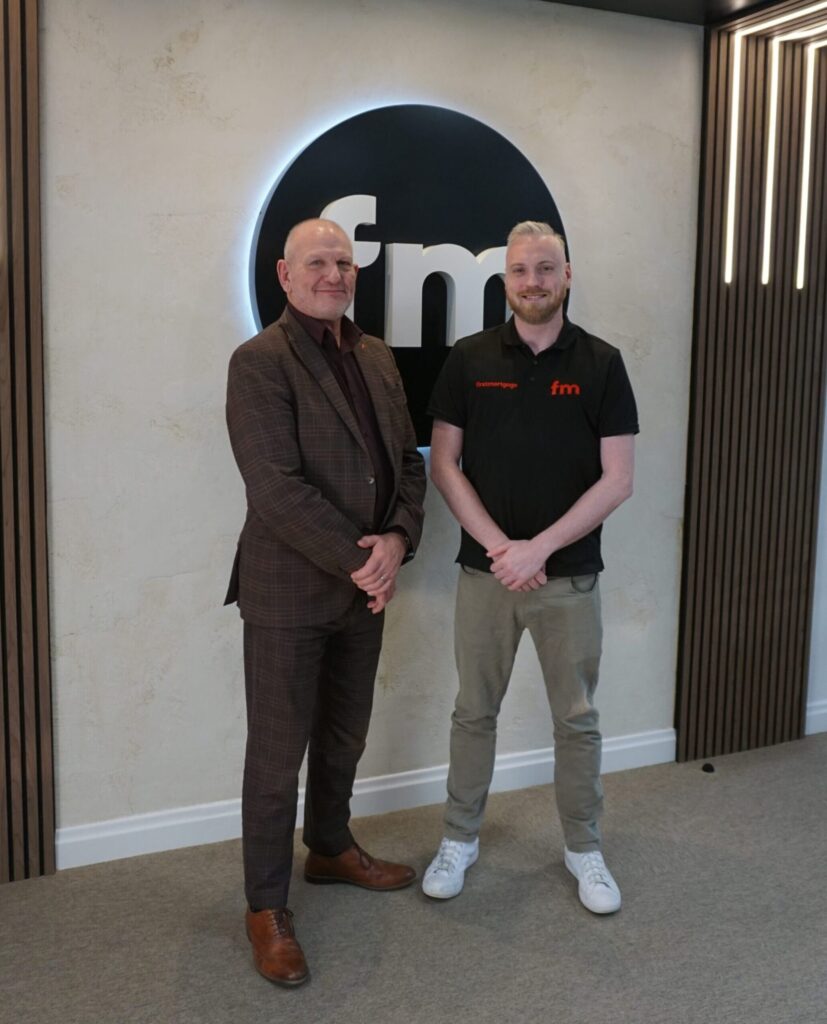 Two men standing in front of Smart IT logo at office.