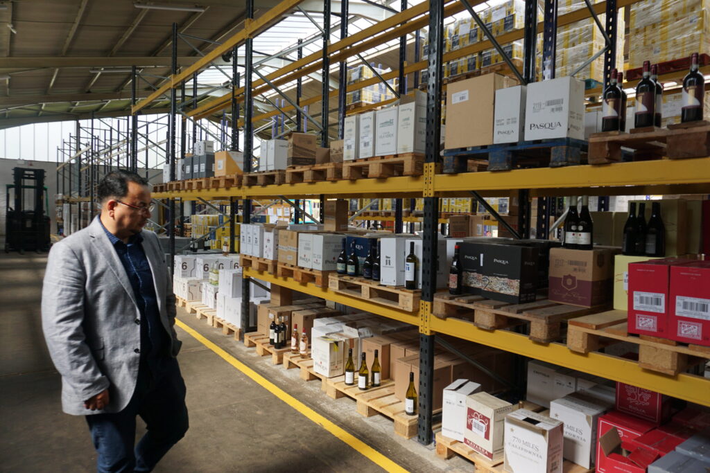 Man inspecting wine bottles and boxes on warehouse shelves.