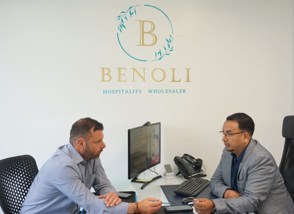 Business meeting at Benoli Wholesale office with two men discussing.