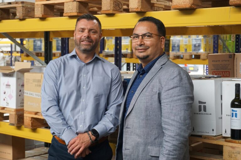 Two men in business attire in a warehouse with shelves and boxes.