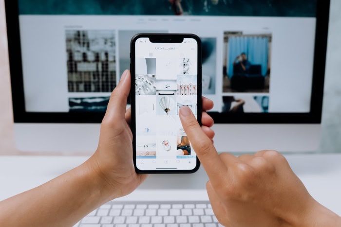 Person using smartphone to browse website on desktop monitor.